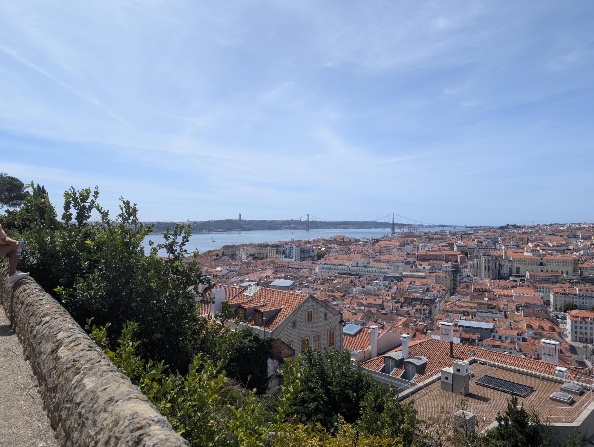 Man sieht die Dächer von Lissabon vom Blick über Lissabon vom Castelo de São Jorge aus. Im Hintergrund sind der Tajo, die Ponte 25 de Abril und Santuário de Cristo Rei sichtbar
